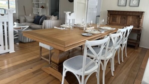 A dining area with a wooden table set for six, surrounded by white chairs.