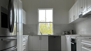 A modern kitchen with white cabinetry, stainless steel appliances, and a large window.