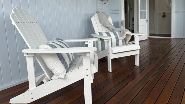 Two white Adirondack chairs with striped cushions, a life ring on the wall, and a wooden deck.