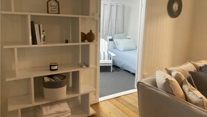 A room with a white shelving unit, a grey sofa, and a bed with striped bedding.