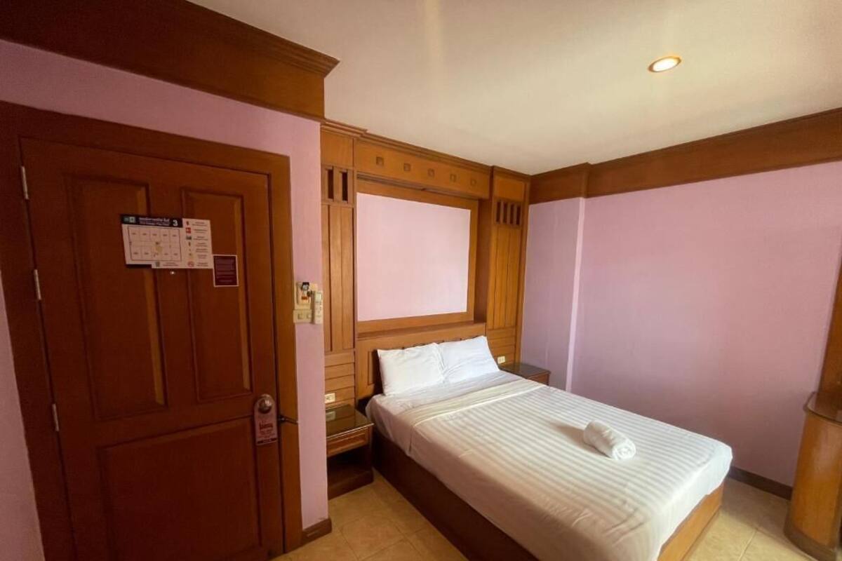 A hotel room with a wooden door, a bed with white bedding, a nightstand, and a wooden headboard.