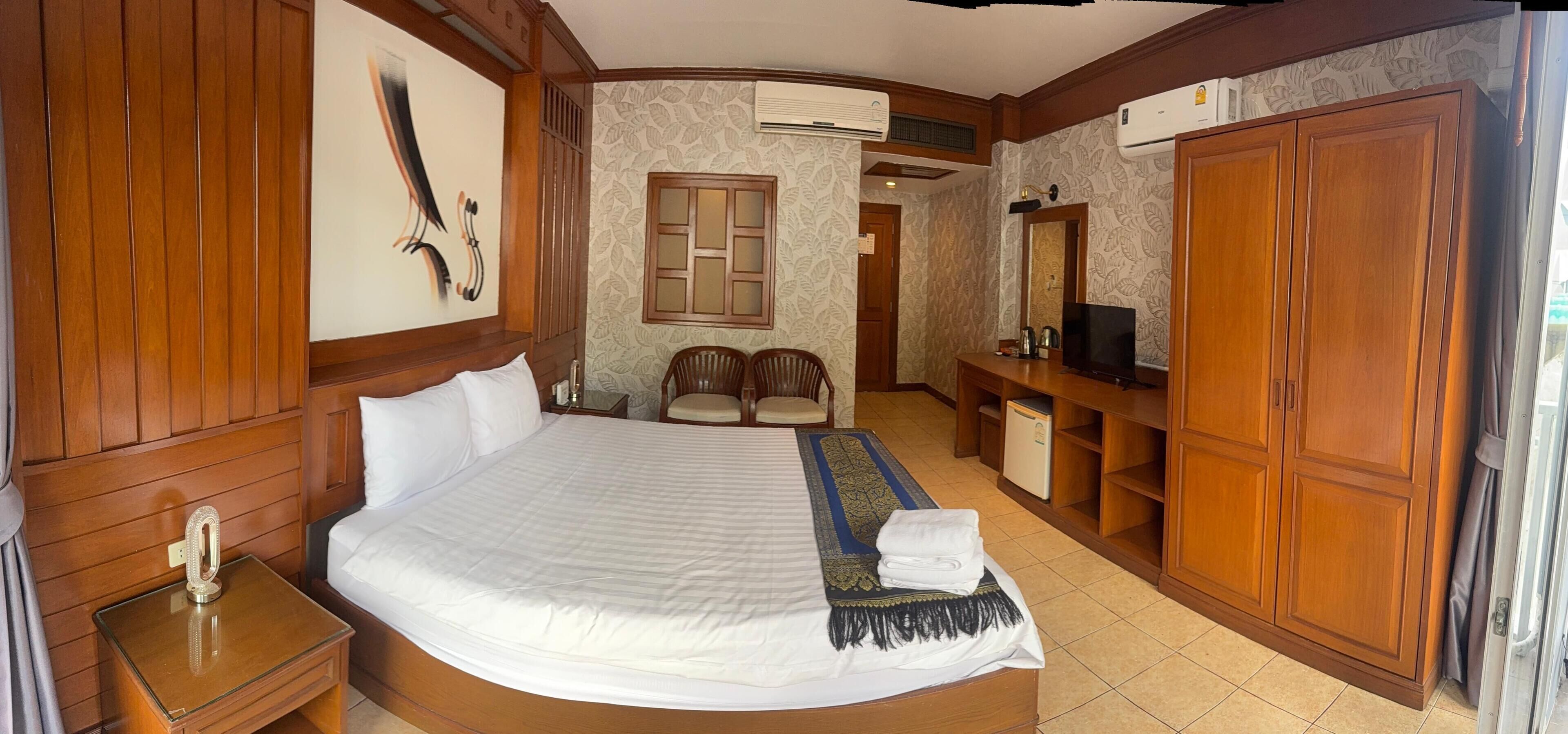 A hotel room with a large bed, wooden furniture, a television, and a wardrobe.