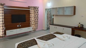 A hotel room with a large bed, a TV mounted on the wall, a minibar, and a small desk with a mirror. - TIO HOTELS & RESORTS - YERCAUD  (Yercaud)