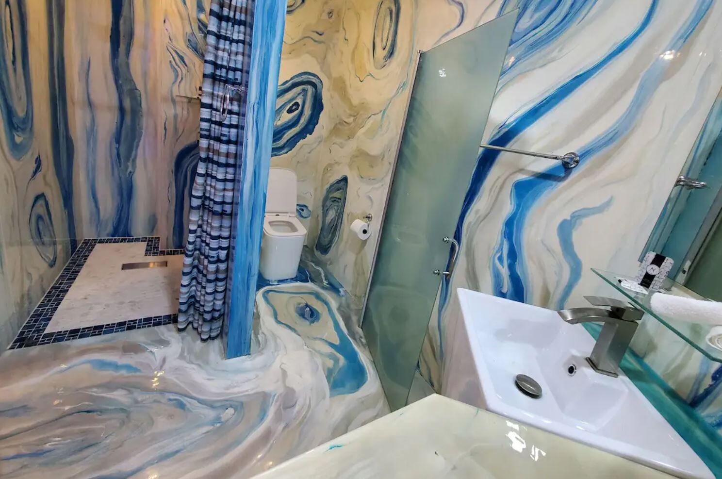 A bathroom with a marble design, a glass shower enclosure, and a white sink.