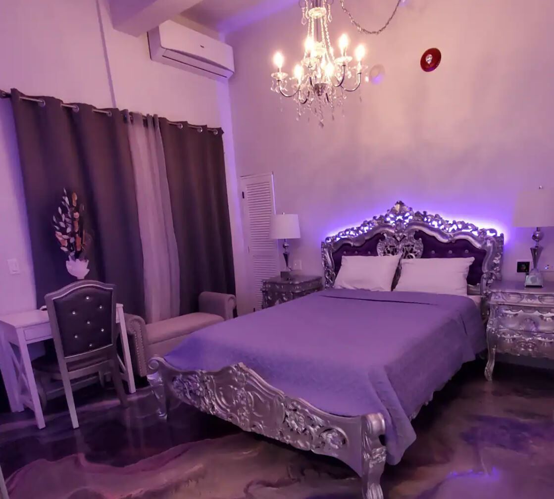 A bedroom with a large bed, a chandelier, a chair, and a nightstand.