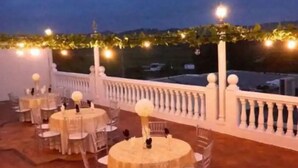 En terrasse med runde borde og stole, pyntet med lyskæder og hvide søjler.