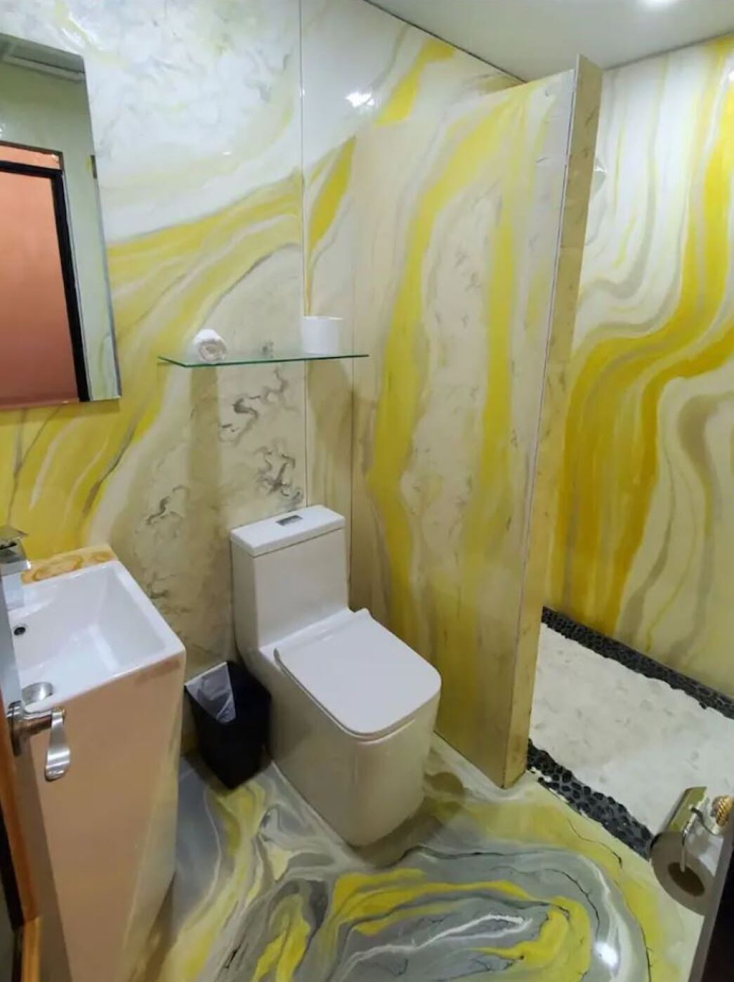 A bathroom with a marble wall, a glass shower enclosure, and a white toilet.