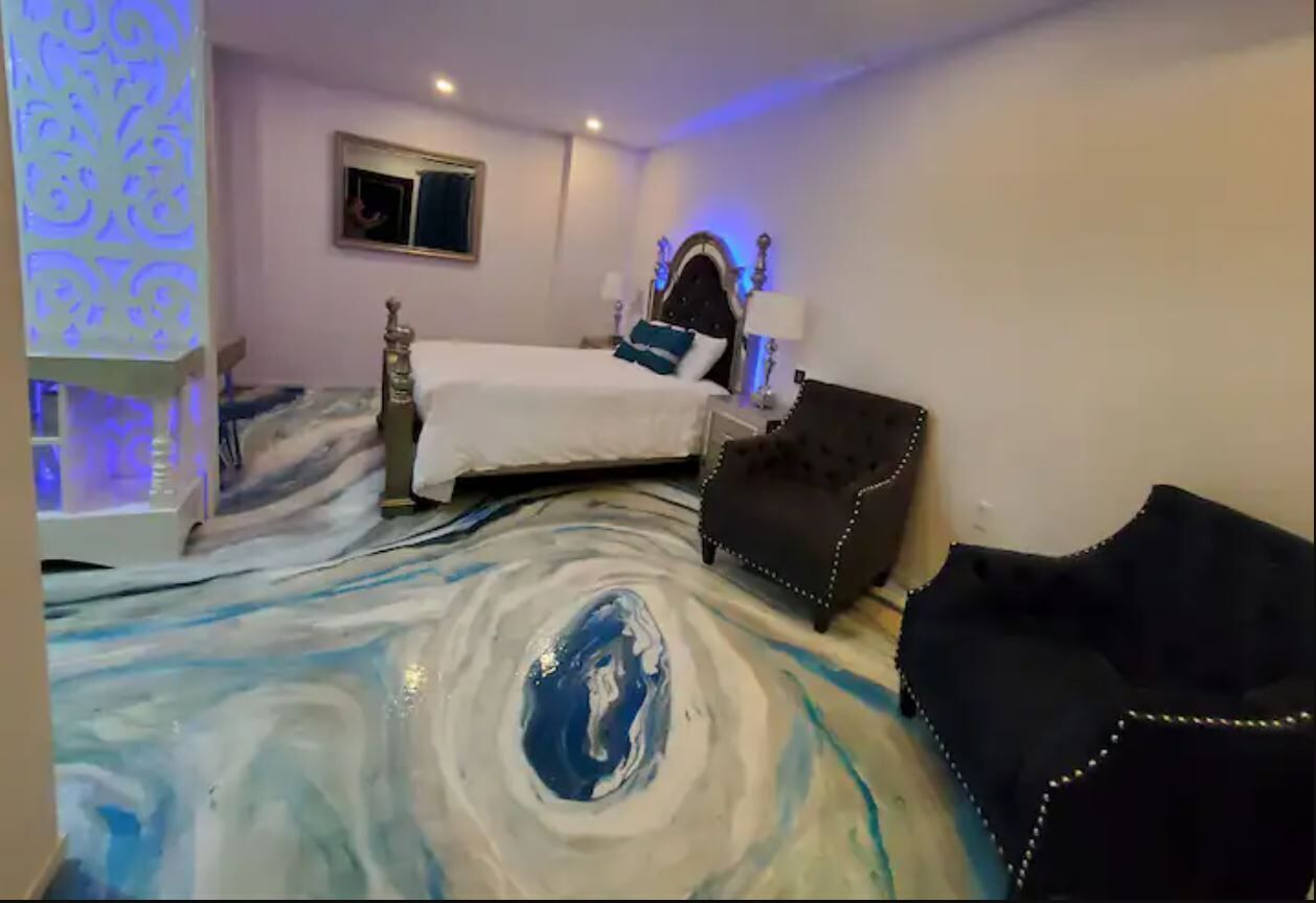 A hotel room with a bed, a black armchair, and a unique marble floor design.