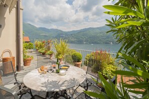 A terrace with a round table set for dining, surrounded by potted plants and a view of a lake and mountains. - Vista Lario in Carate Urio (Carate Urio)