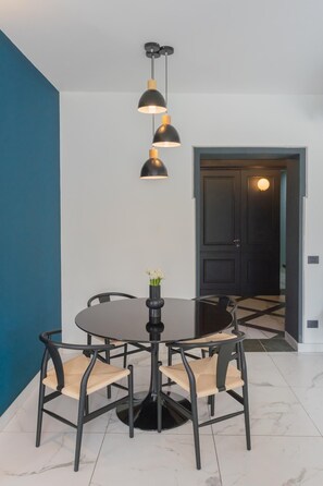 Uma sala de jantar com uma mesa redonda, quatro cadeiras e um lustre pendente preto.