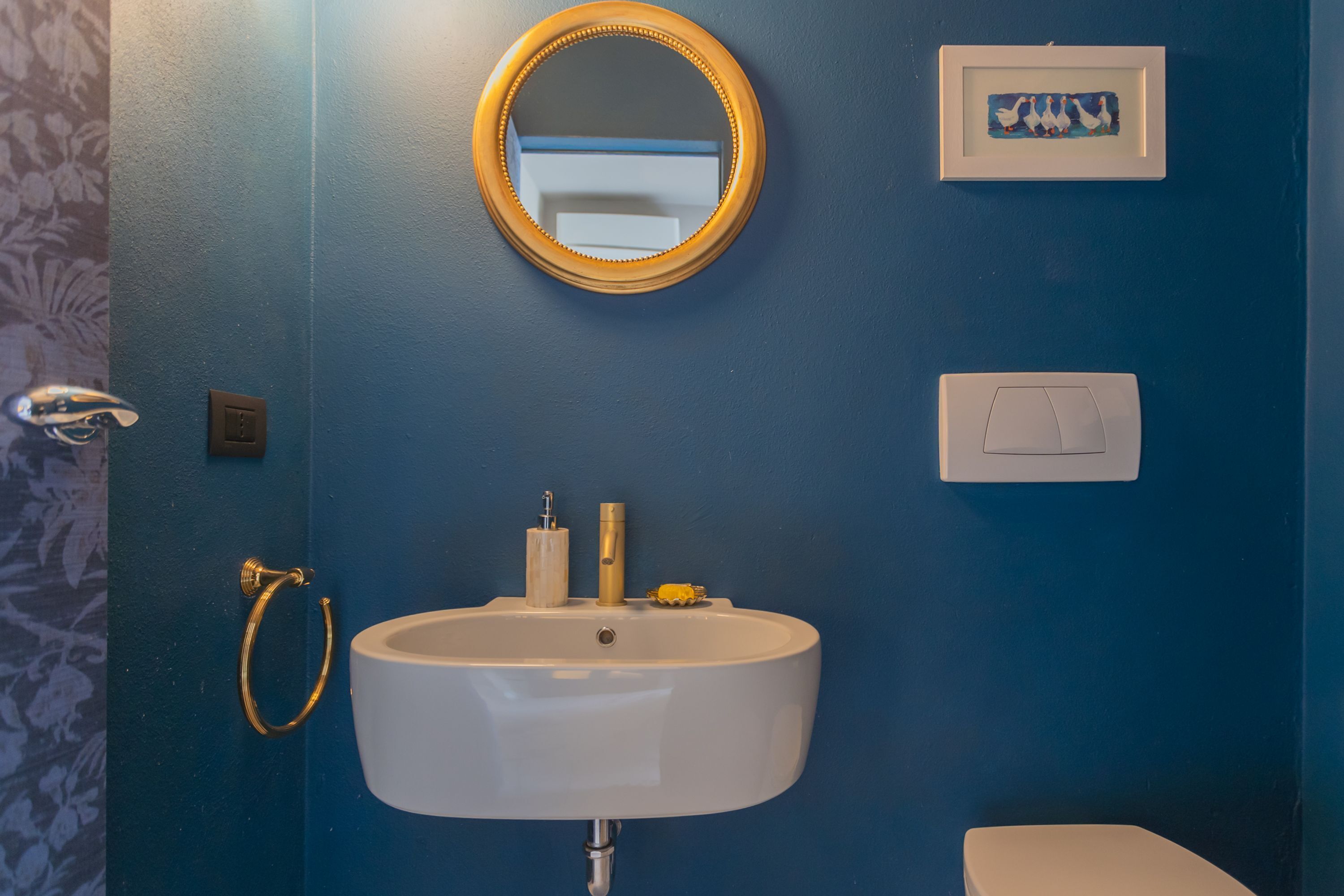 A bathroom with a white sink, gold towel ring, and a round mirror.