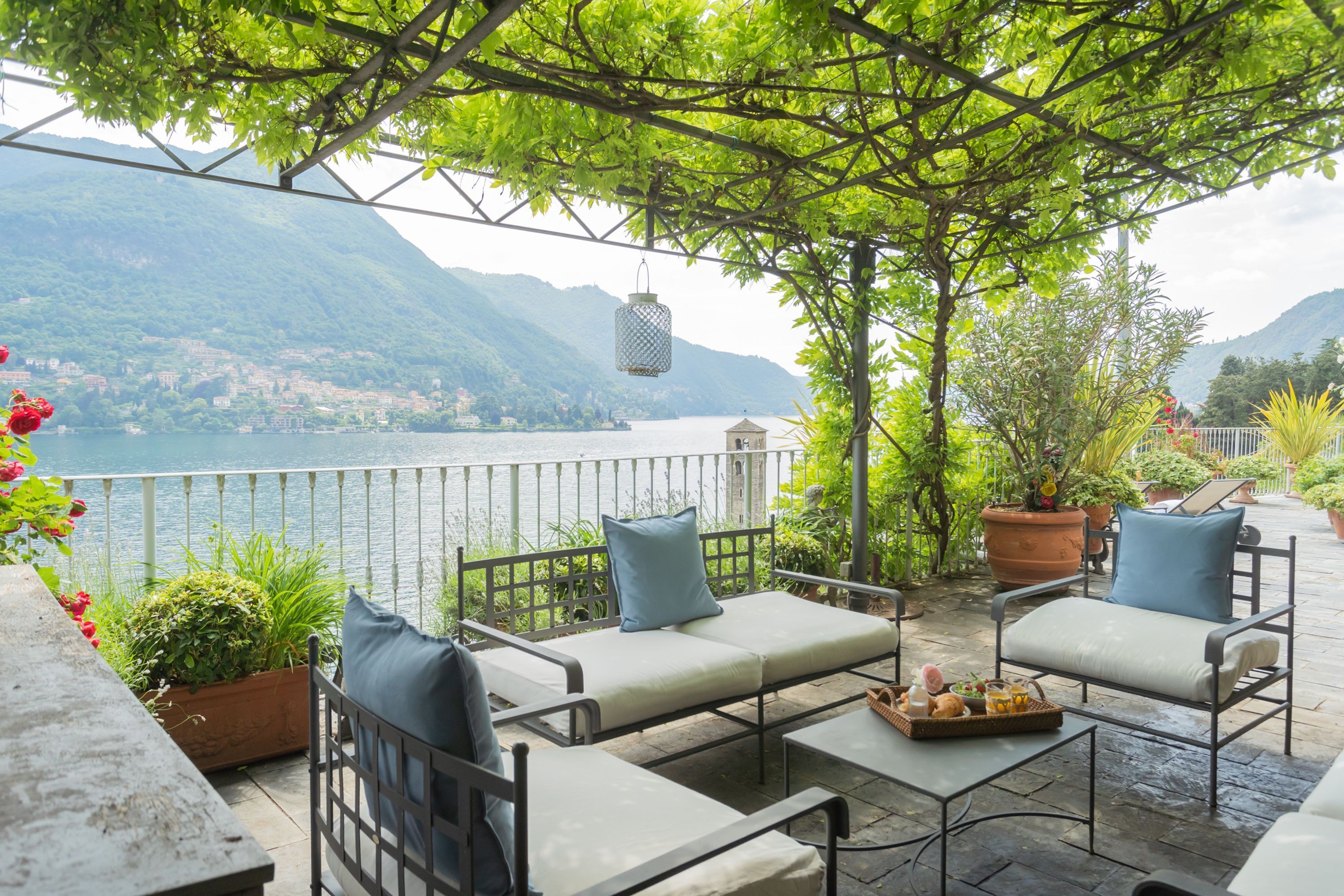 A terrace with outdoor seating, a view of a lake, and mountains in the background.