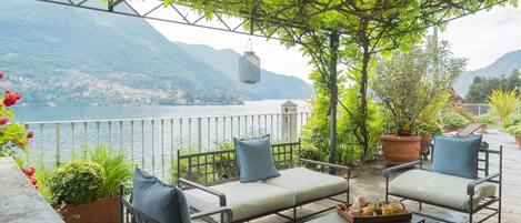 A terrace with outdoor seating, a view of a lake, and mountains in the background.