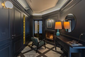 Une pièce aux couleurs sombres, avec une cheminée, un fauteuil bleu et un bureau doté d’une lampe.