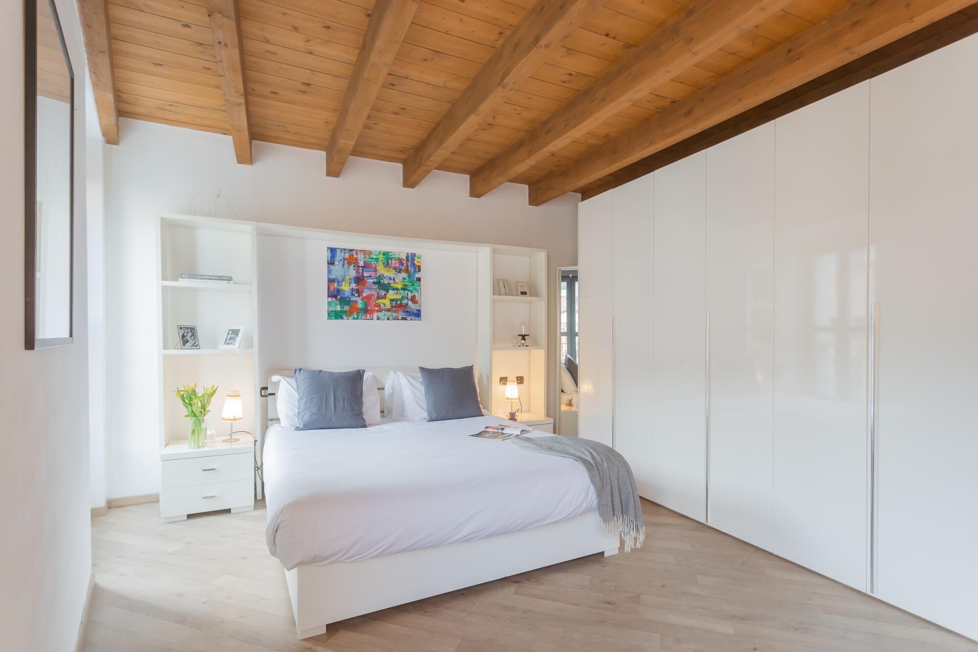 A bedroom with a bed, white wardrobe, and a colorful abstract painting on the wall.