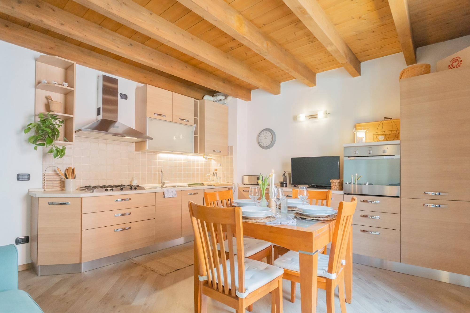 Una cocina moderna con armarios de madera, una mesa de comedor lista para cuatro comensales y un horno empotrado.