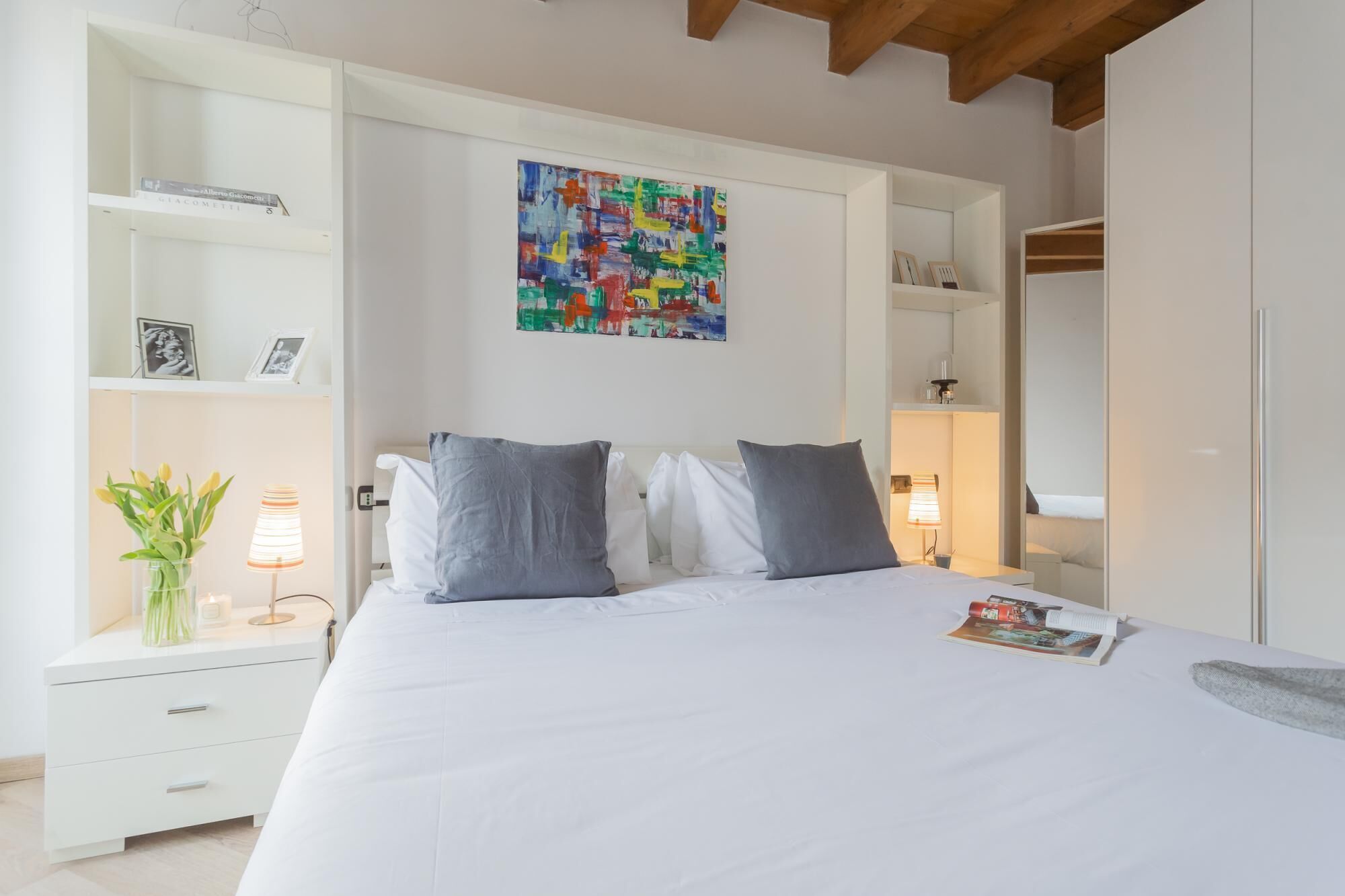 A bedroom with a bed, bedside tables, a nightstand, a painting, and a wardrobe.