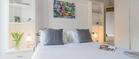 A bedroom with a bed, bedside tables, a nightstand, a painting, and a wardrobe.