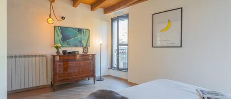 A bedroom with a wooden ceiling, a bed with a white sheet, a framed picture of a banana, a dresser, and a painting on the wall.