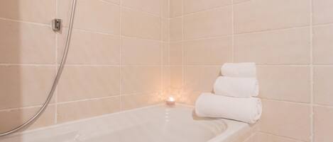 A bathroom with a bathtub, a shower, and a lit candle.