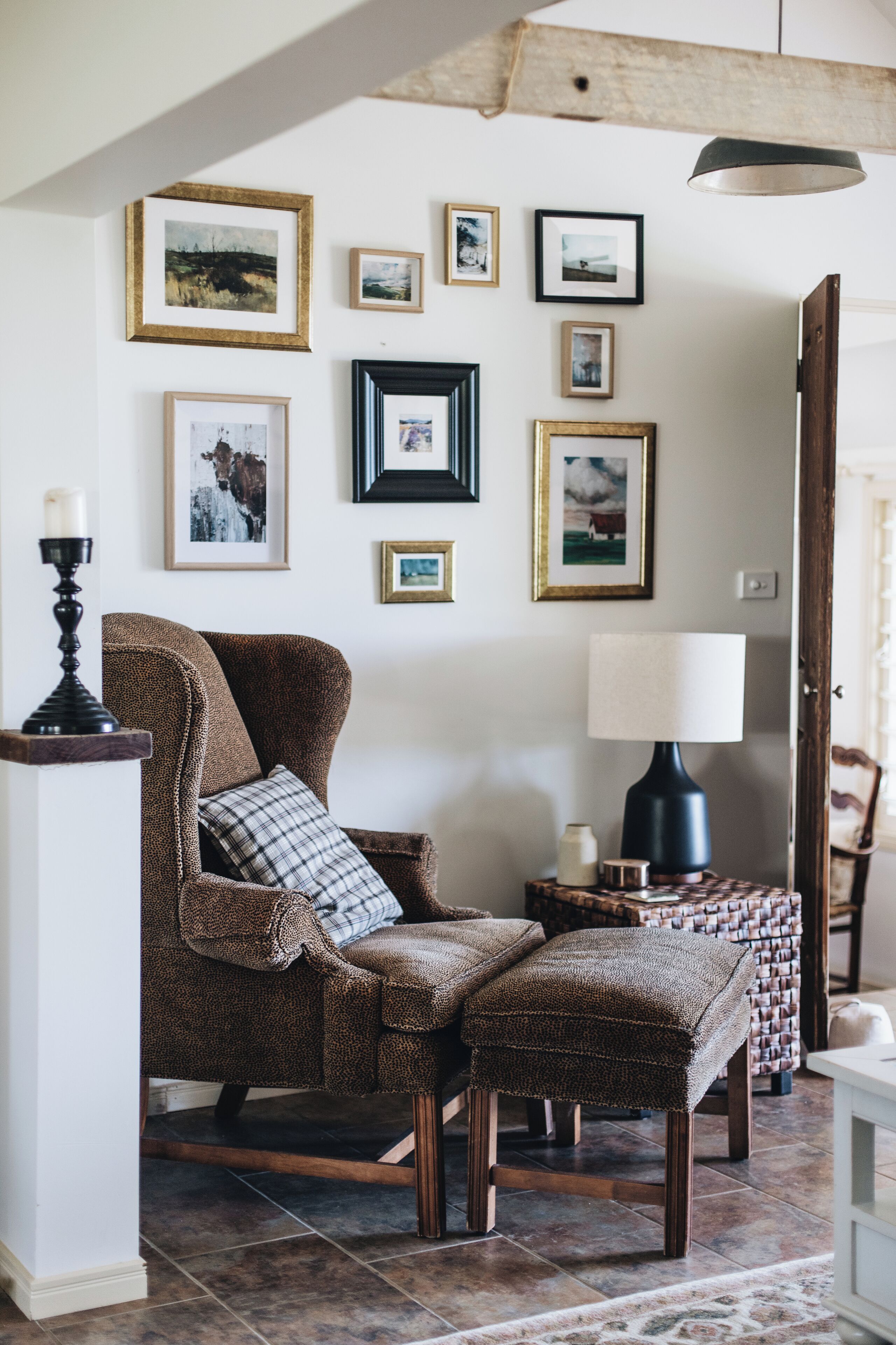 A cozy room with a brown armchair, a matching ottoman, a side table with a lamp, and a wall adorned with framed pictures.
