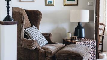 A cozy room with a brown armchair, a matching ottoman, a side table with a lamp, and a wall adorned with framed pictures.