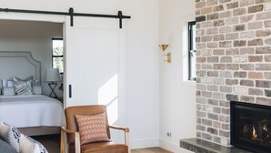 A modern room with a bed, a sofa, a chair, a fireplace, and a brick wall.