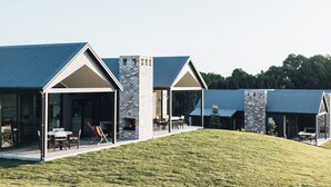 A modern building with a covered patio area, a stone fireplace, and a grassy lawn.