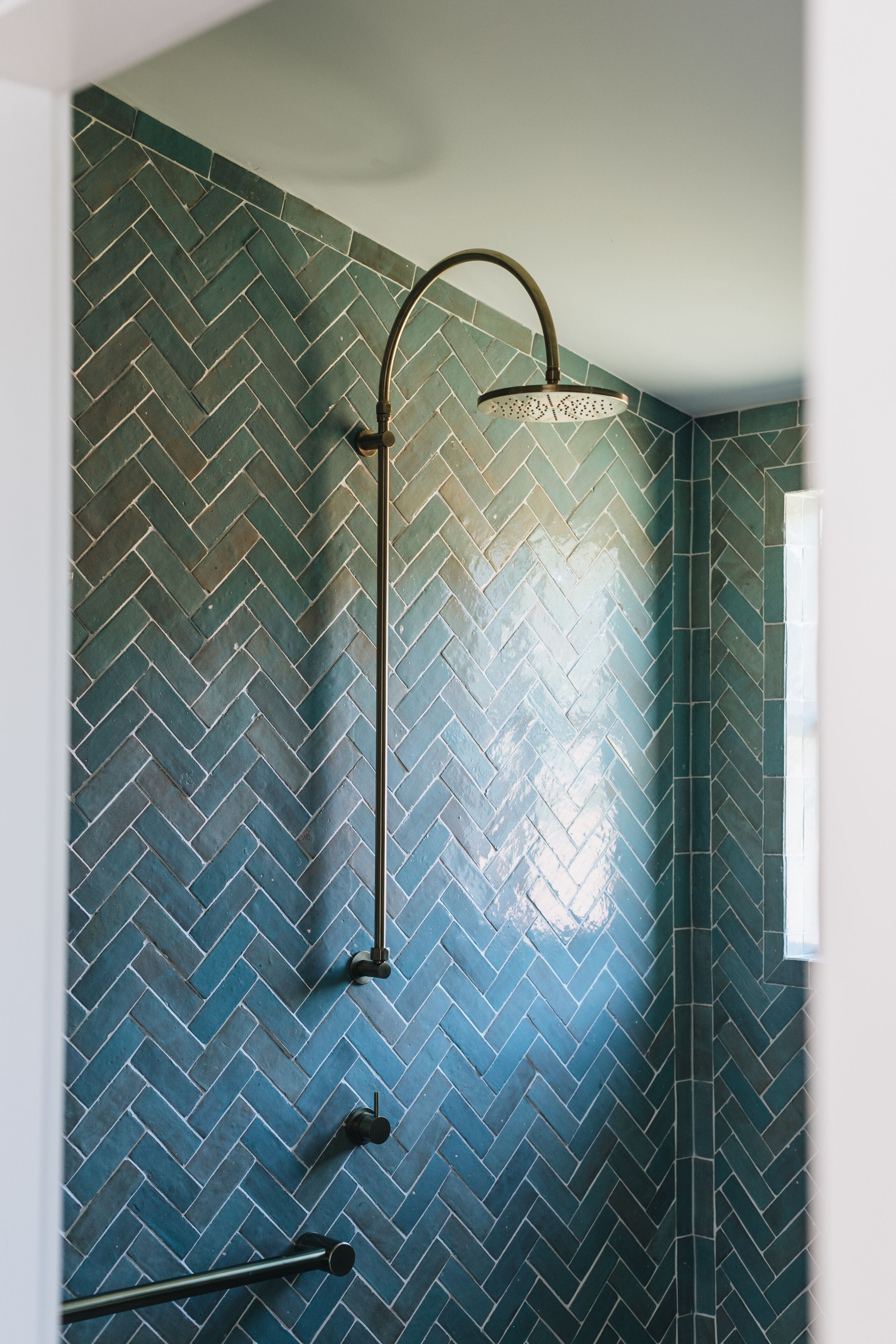A shower with a curved showerhead and a herringbone tile pattern on the walls.