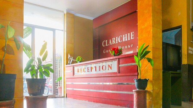 Un espace d’accueil avec un comptoir rouge portant l’inscription « CLARICHIE, maison d’hôtes » et une enseigne au-dessus. De part et d’autre du comptoir, on trouve des plantes en pot.