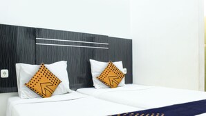 Une chambre d’hôtel au design moderne, dotée d’un grand lit avec une literie blanche, de deux coussins décoratifs à motifs géométriques et d’un plaid bleu foncé.