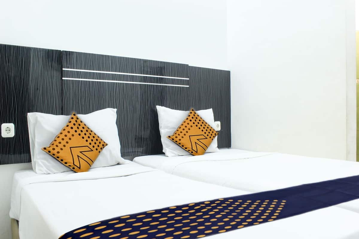 Ein Hotelzimmer im modernen Stil, mit einem großen Bett, weißer Bettwäsche, zwei dekorativen Kissen mit geometrischem Muster und einer dunkelblauen Tagesdecke.