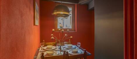 A dining area with a table set for four, a chandelier, and a window with a view.