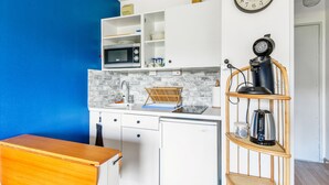 Eine kompakte Küche mit weißen Schränken, einer Mikrowelle, einem Spülbecken und einer Kaffeemaschine.