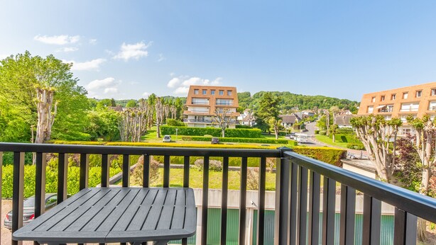 Ein Balkon mit Tisch und Stühlen, der auf einen Wohnbereich mit Häusern und Grünflächen blickt.