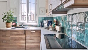 A modern kitchen with wooden cabinets, a built-in stove, and a window with a view of buildings. - Appartement Chernoviz - Welkeys (Paris)