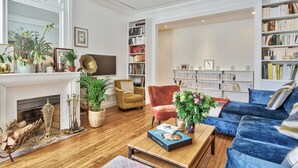 A spacious living room with a fireplace, a bookshelf, a blue sofa, and a coffee table. - Appartement Chernoviz - Welkeys (Paris)