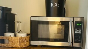 A microwave oven with a digital display, a black container labeled 'ice' on top, and a wicker basket with two white mugs on a wooden shelf. - Wilton Manors Guesthouse #4 (Wilton Manors)