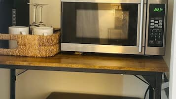 A microwave oven with a digital display, a black container labeled 'ice' on top, and a wicker basket with two white mugs on a wooden shelf.