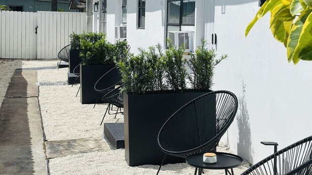 A modern building with a white exterior, large windows, and outdoor seating with black chairs and planters. - Wilton Manors Guesthouse #4 (Wilton Manors)
