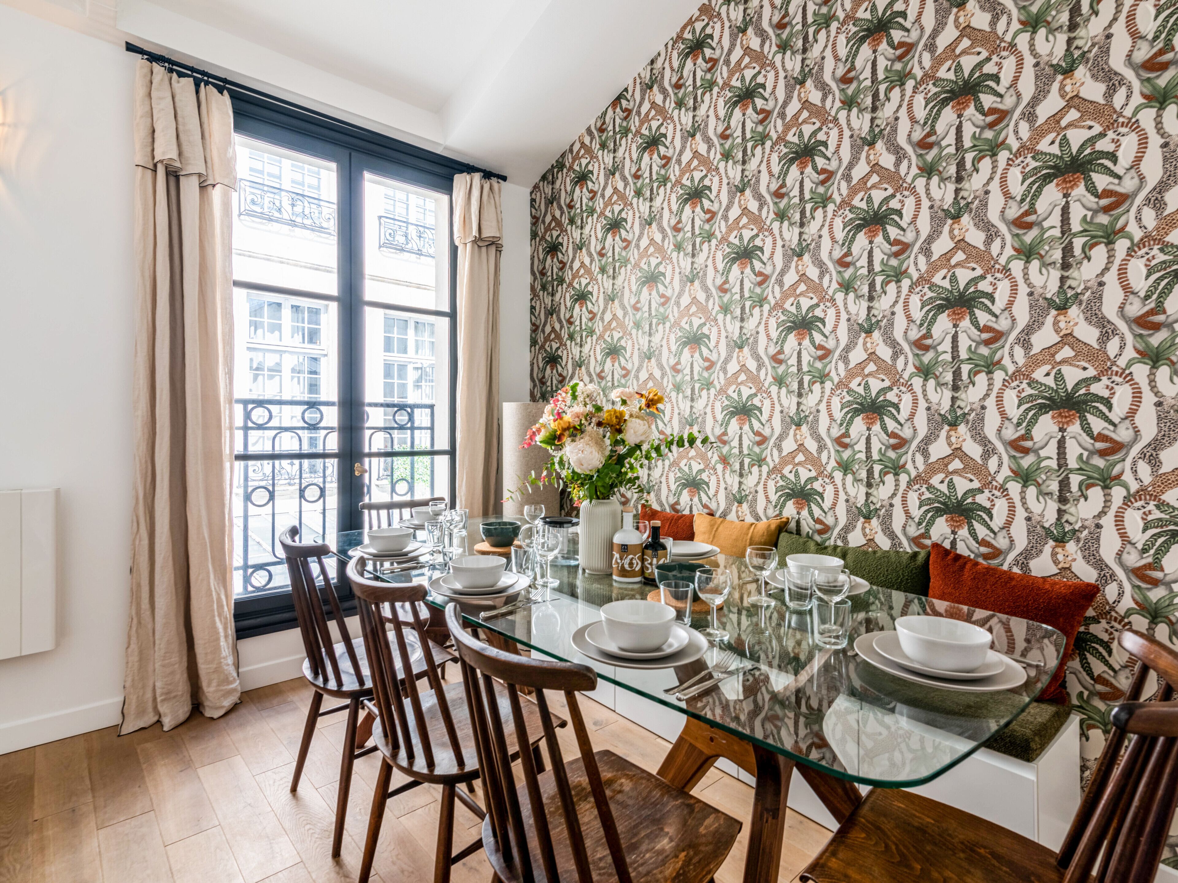 A dining area with a glass table, wooden chairs, and a patterned wallpaper.