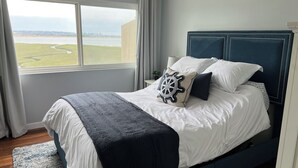 A bedroom with a large bed, a view of a body of water, and a cityscape in the distance. - Paradise on the bay - Luxury condo (San Diego)