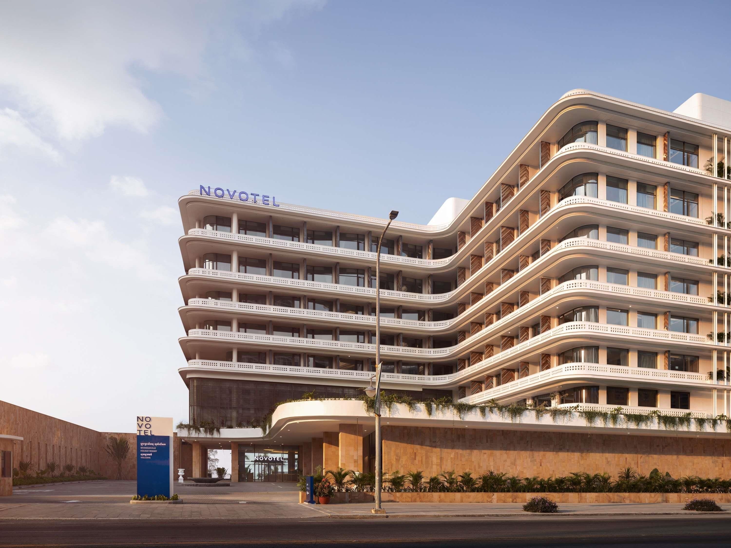 A multi-story hotel with a curved facade, balconies, and a sign reading 'NOVOTEL'.