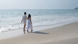 Una pareja caminando sobre una playa arenosa con el océano al fondo.