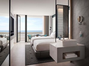 Een moderne hotelkamer met een groot bed, een badkamer met een wastafel en spiegel, een balkon met uitzicht op zee, en een kamerbreed tapijt met een patroon.