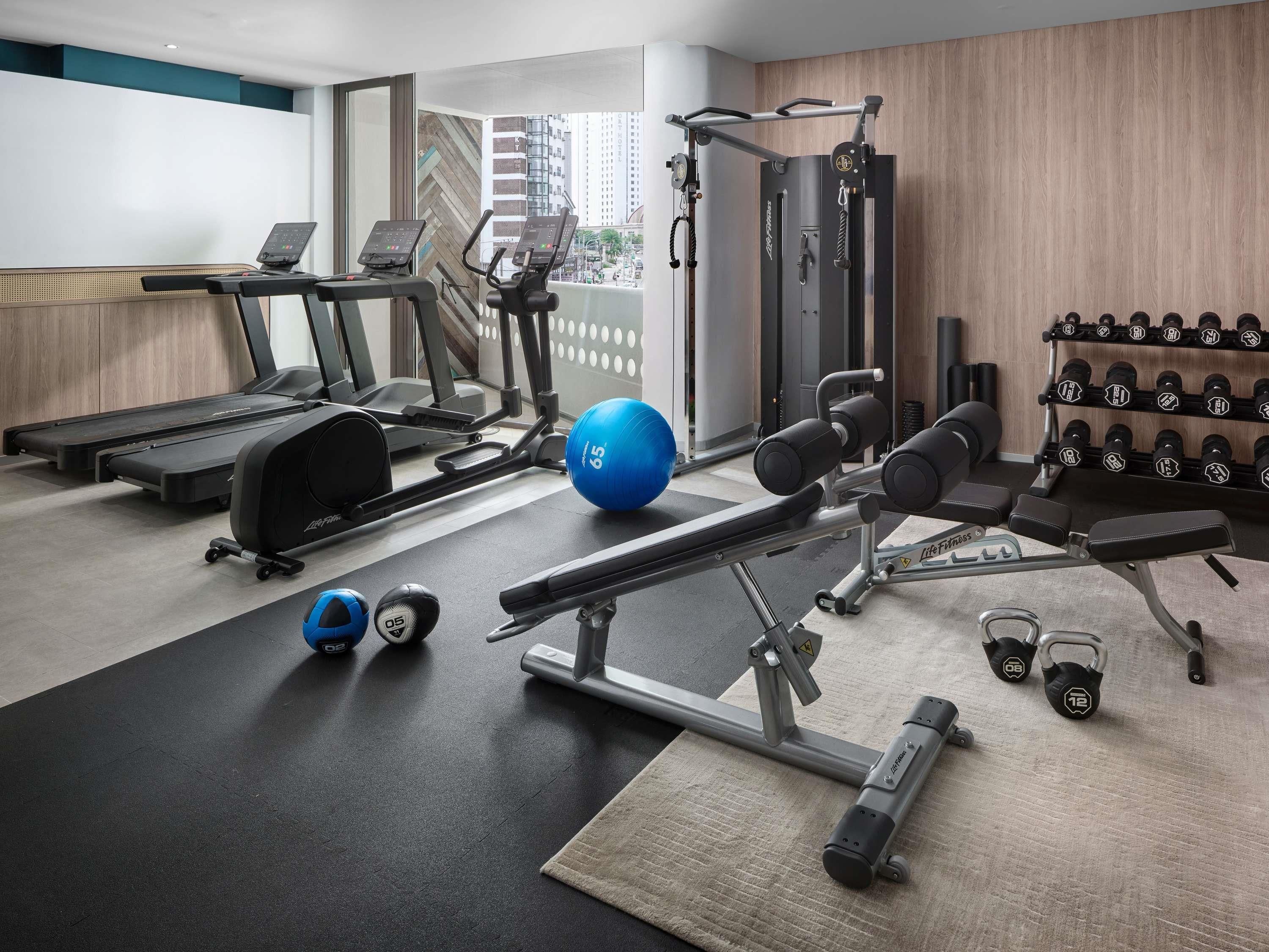 Una palestra con tapis roulant, macchine ellittiche, panca per pesi, manubri e palle per esercizi.
