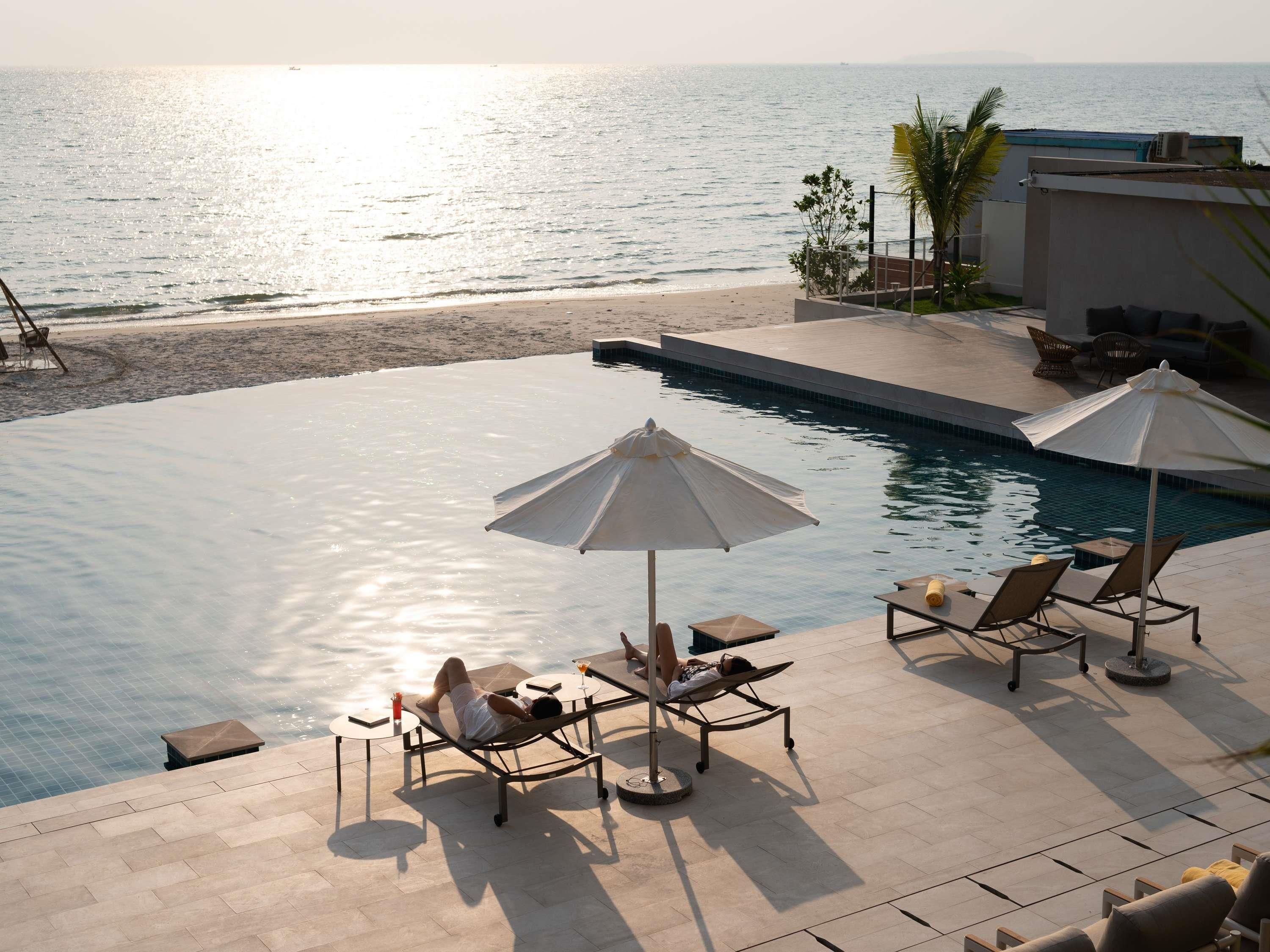 A poolside area with lounge chairs and umbrellas, overlooking a beach and the sea.