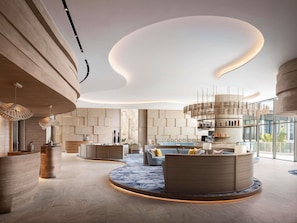 Eine moderne Lobby mit einer zentralen Sitzecke, einer Bar und einem Empfangsbereich.