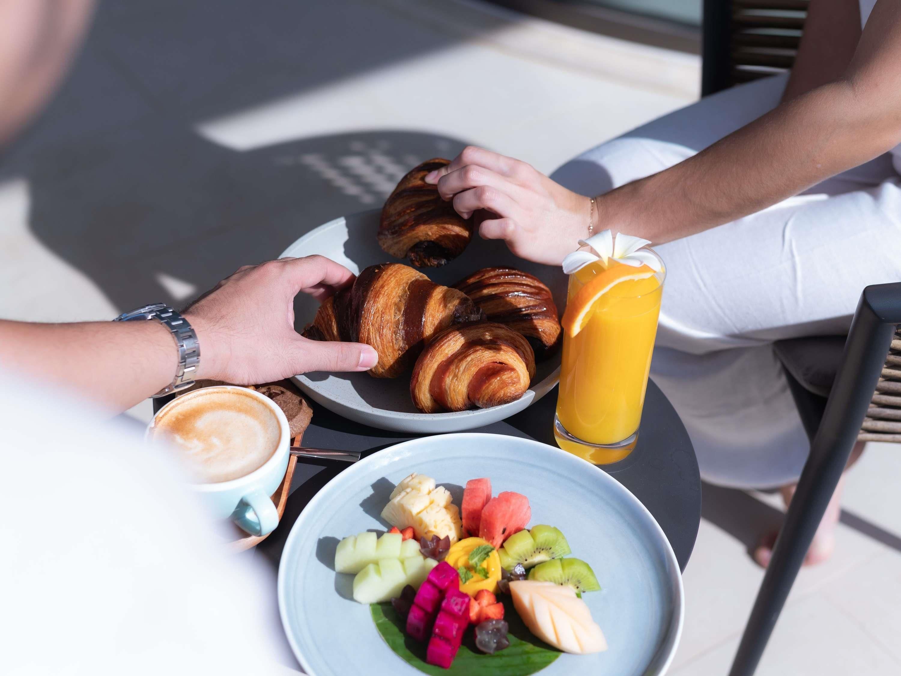A breakfast setting with croissants, fruit, a coffee cup, and a glass of orange juice.