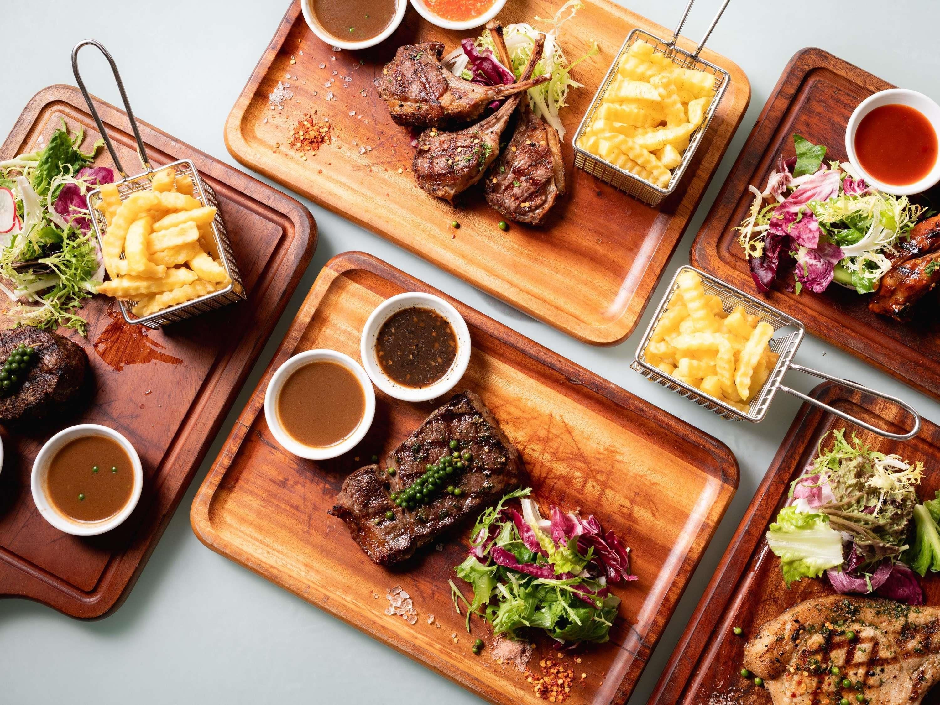A variety of dishes including steaks, fries, and salads on wooden serving boards.